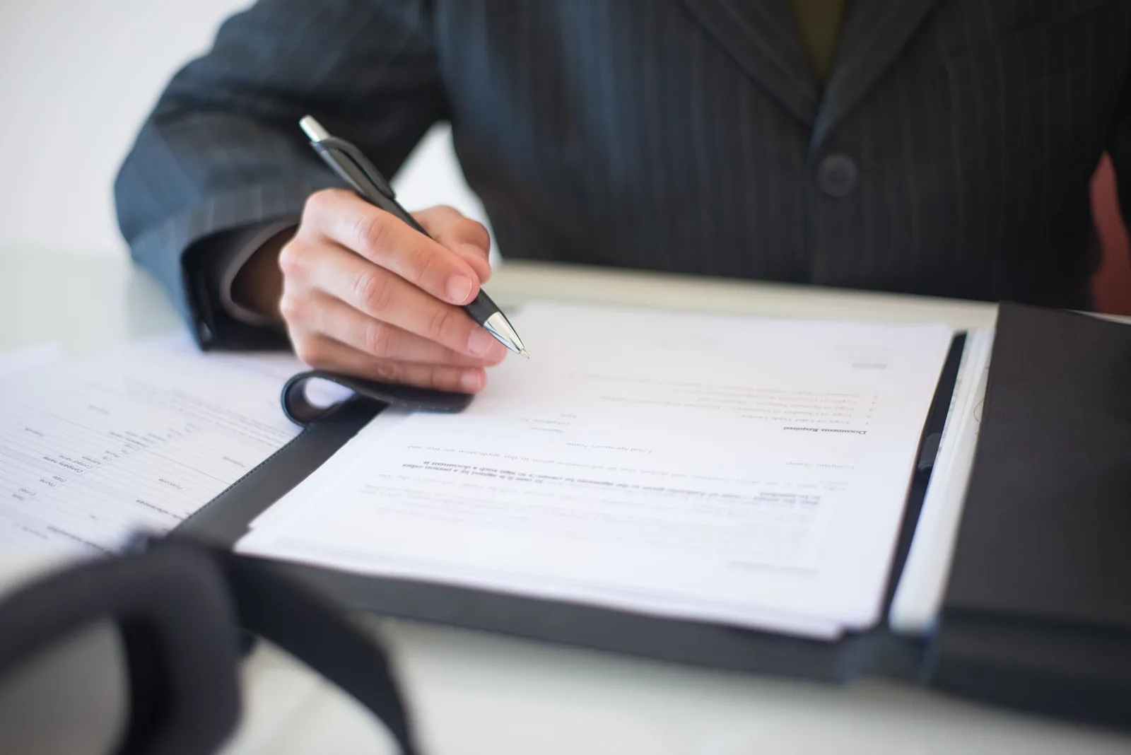 Dirigeant en costume signant un dossier de documents d'entreprise posé dans un classeur sur un bureau
