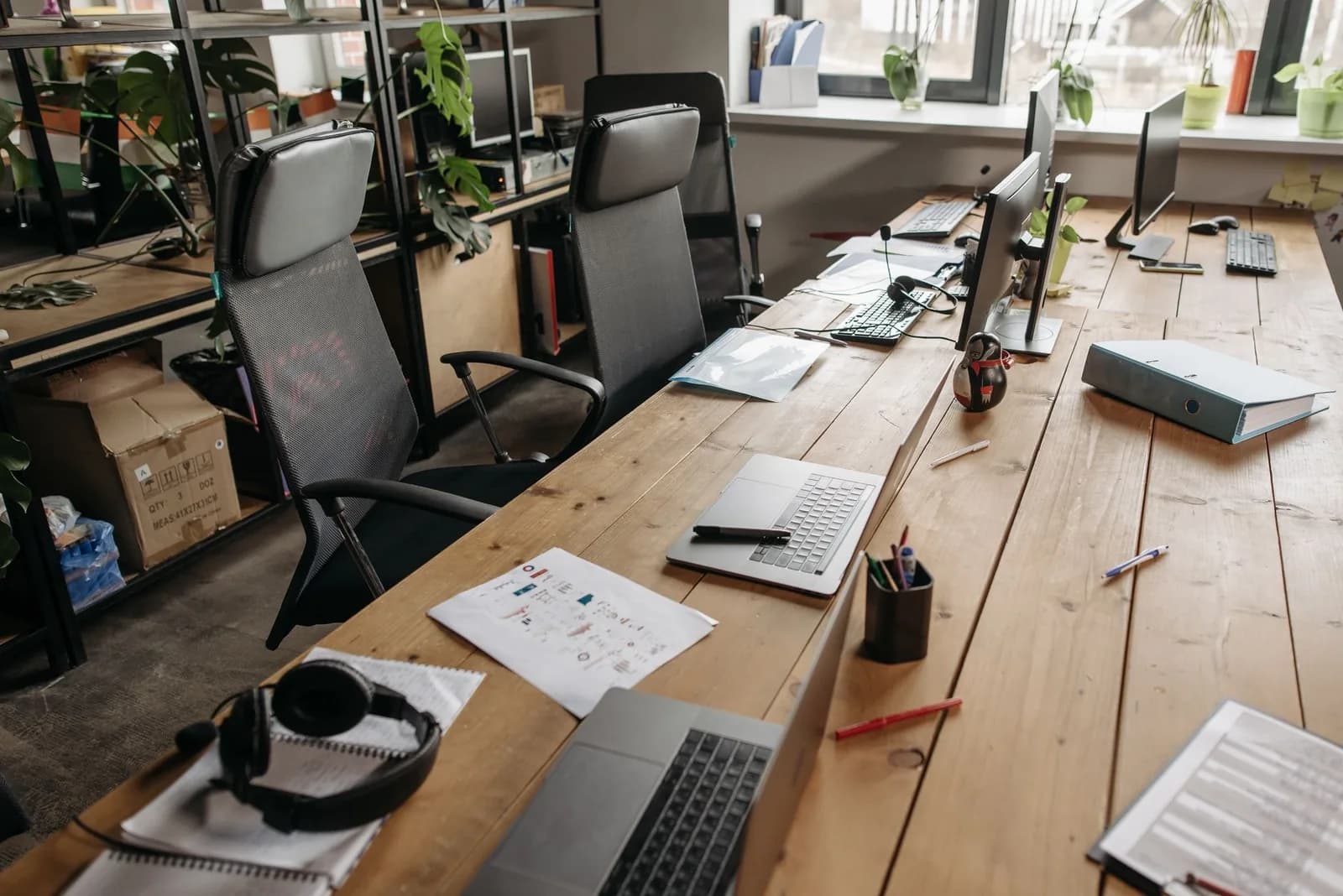Grande table en bois d'un bureau partagé avec ordinateurs portables, écrans, casque et dossiers, sans personne