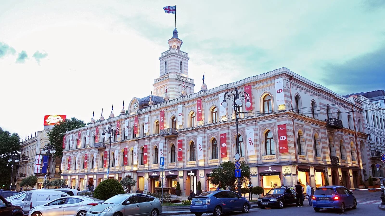 Façade de l'hôtel de ville de Tbilissi, place de la Liberté, au crépuscule, avec le drapeau géorgien sur la tour