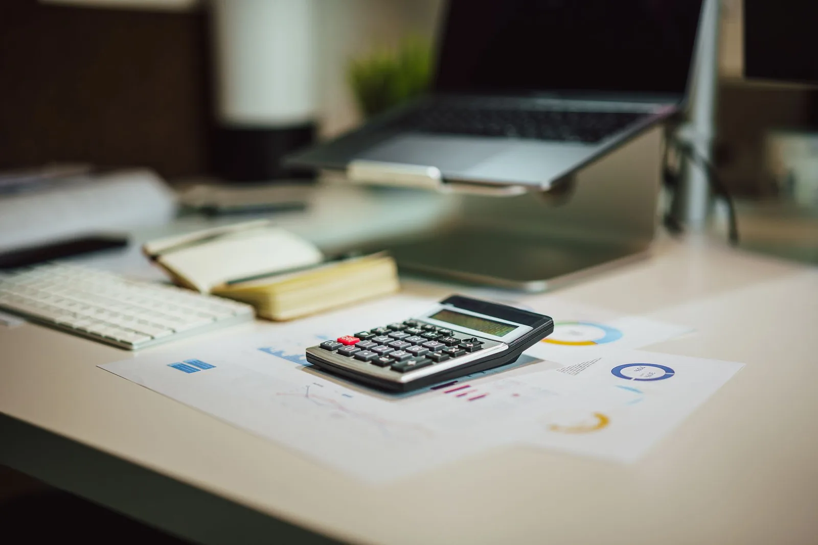 Calculatrice posée sur des documents chiffrés, avec un ordinateur portable sur un bureau