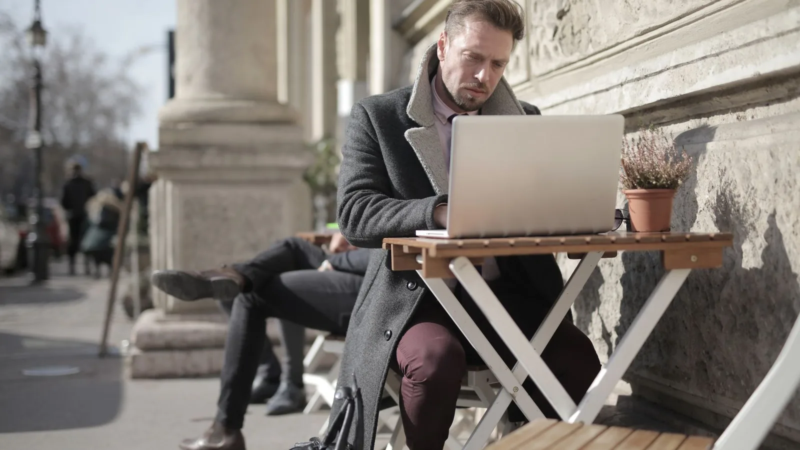 Entrepreneur indépendant travaillant sur son ordinateur portable à une table de café en terrasse.