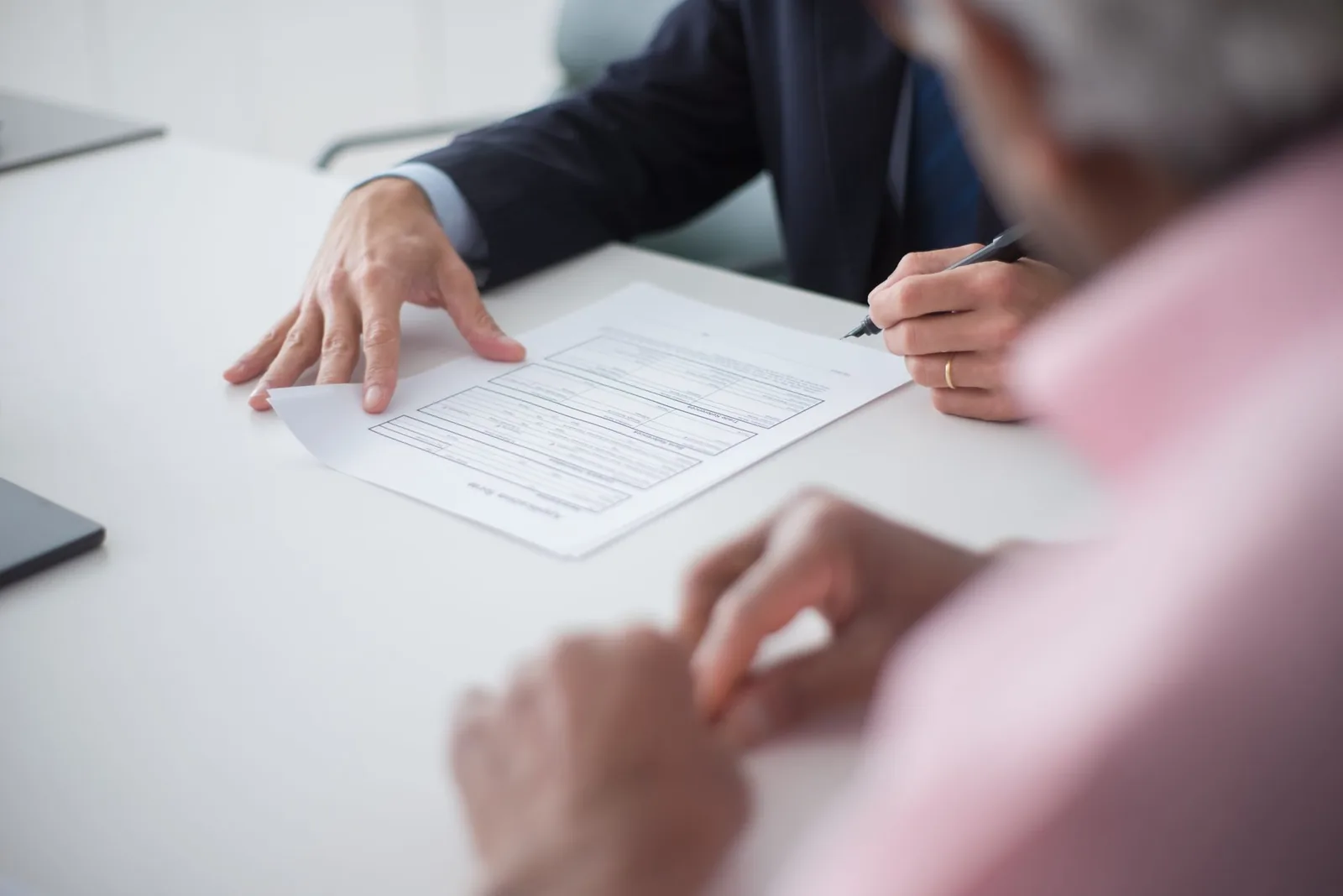Un conseiller en costume et un client signent un formulaire posé sur une table de bureau, mains au premier plan