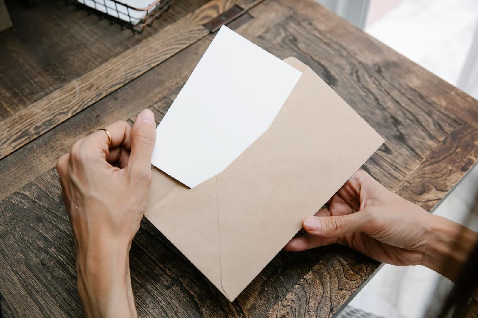 Mains sortant une feuille d'une enveloppe kraft sur un bureau en bois, dossier administratif