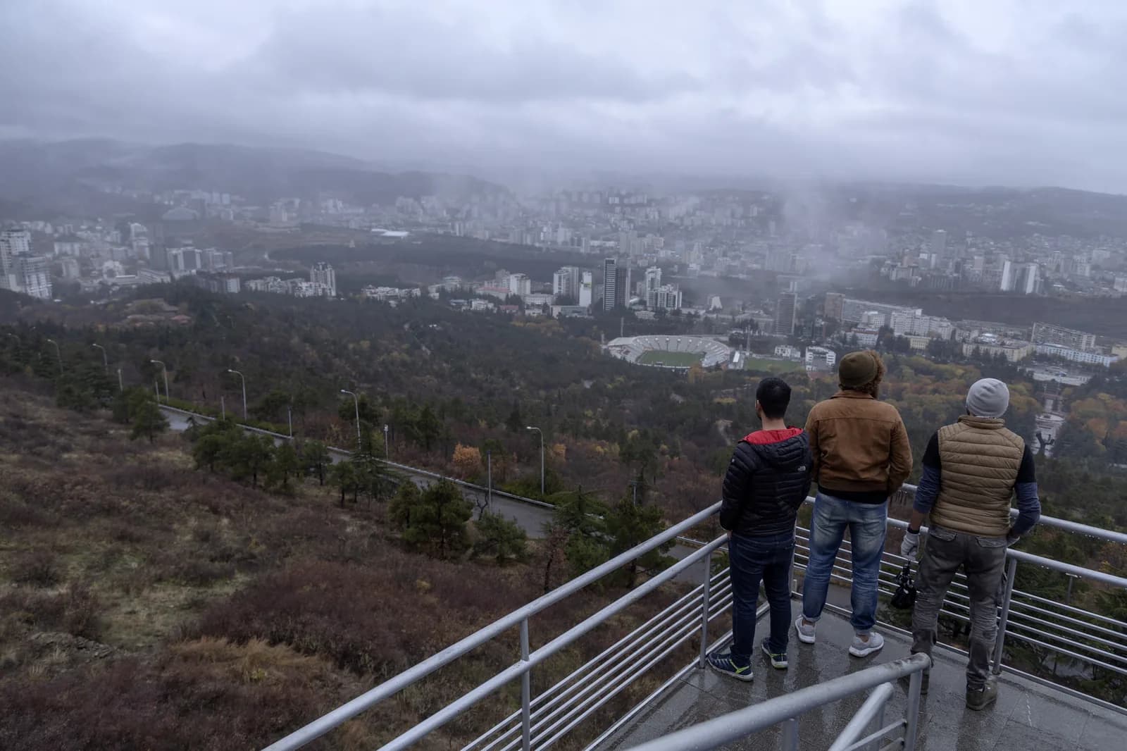 Trois visiteurs sur un belvédère du parc Vake, avec les quartiers résidentiels de Tbilissi en contrebas
