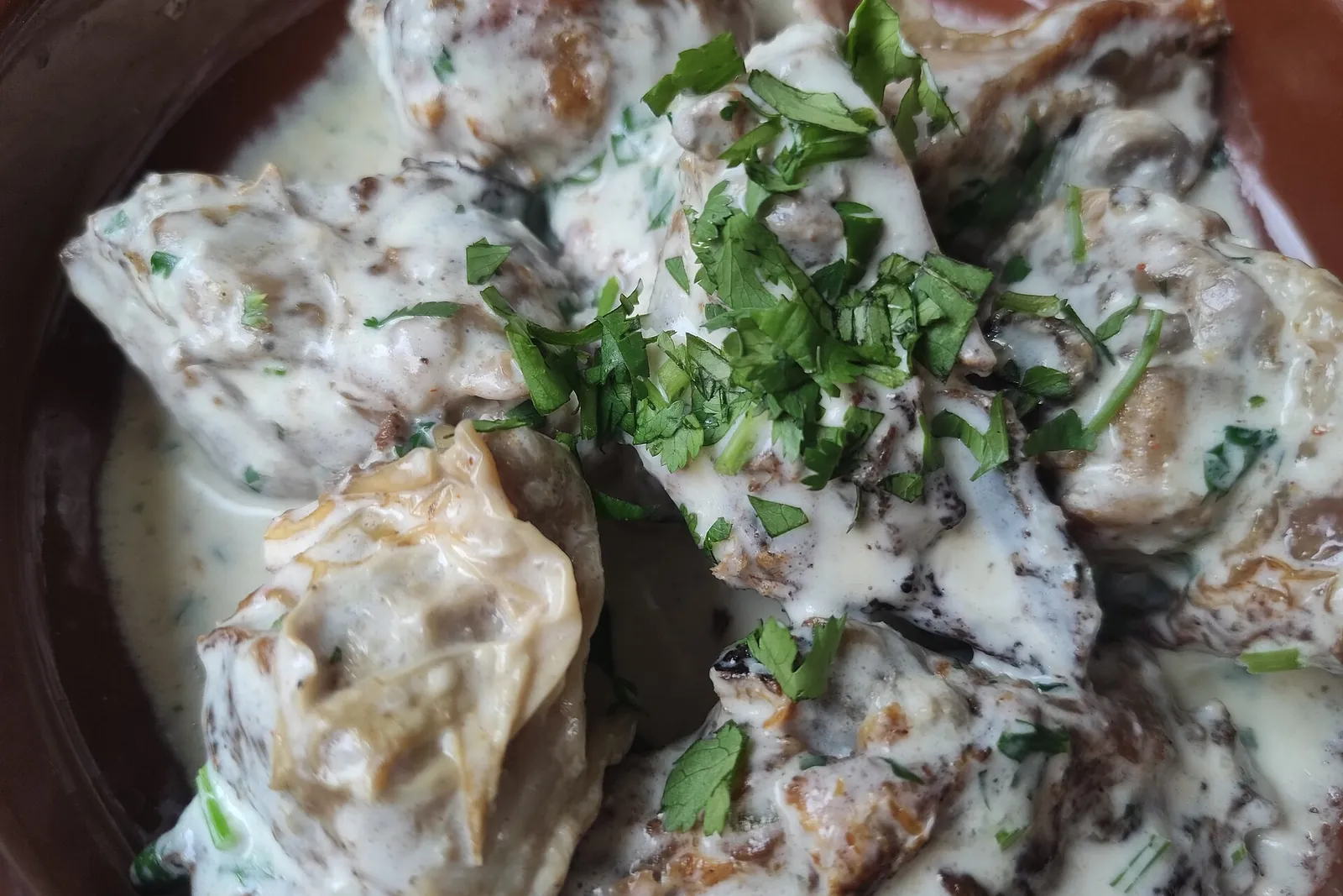 Chkmeruli, morceaux de poulet nappés d'une sauce crémeuse à l'ail et parsemés d'herbes fraîches, dans un plat en terre cuite