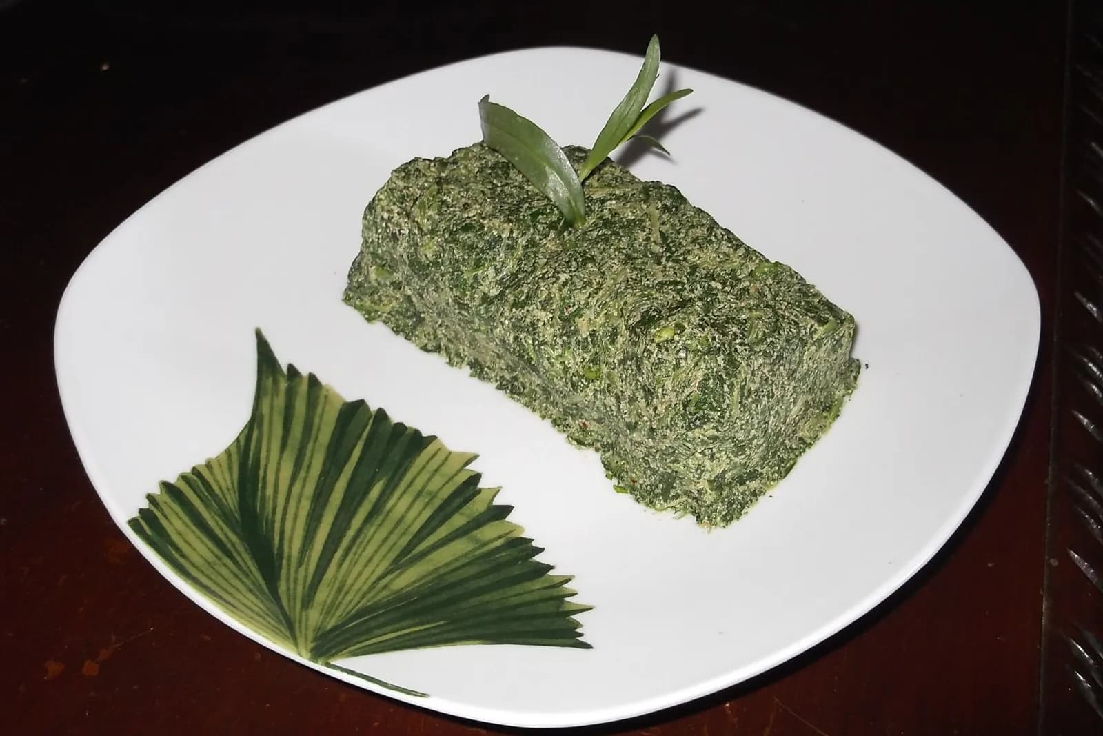 Pkhali aux épinards et aux noix, moulé en rectangle sur une assiette blanche, avec un brin d'herbe en garniture