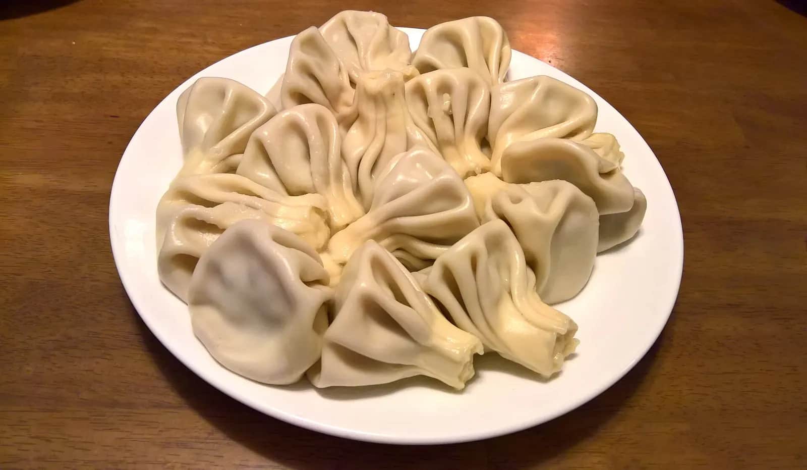 Assiette blanche de khinkali cuits, ces raviolis géorgiens farcis de viande, posée sur une table en bois