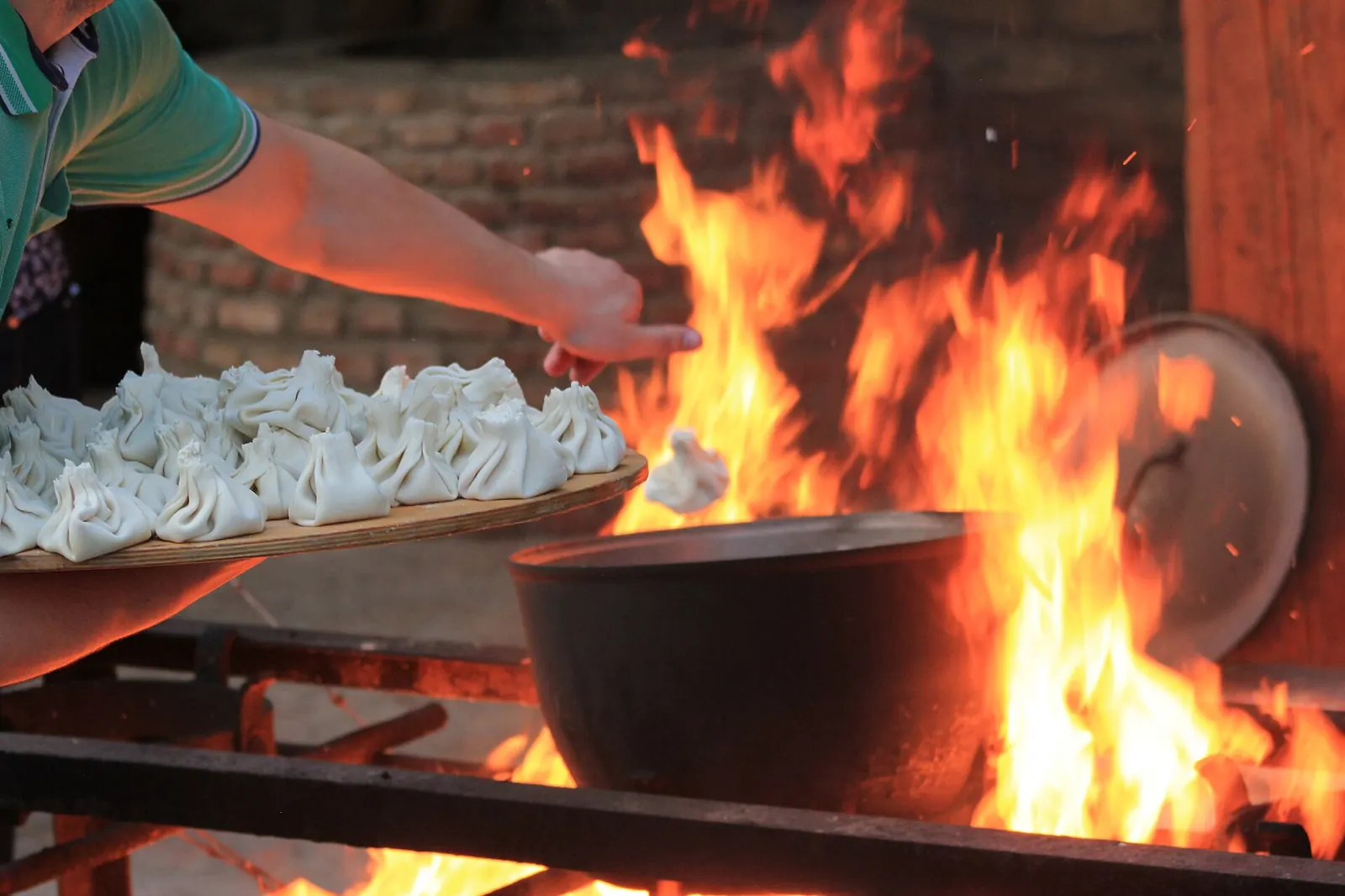 Khinkali crus plongés dans un grand chaudron sur feu de bois, plateau de khinkali à la main