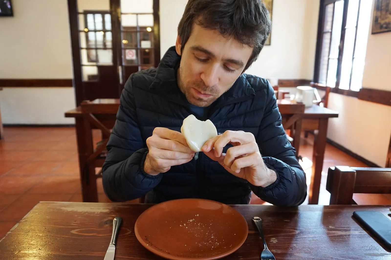 Un convive mange un khinkali à la main, en le tenant par la queue, à une table en bois avec assiette en terre cuite
