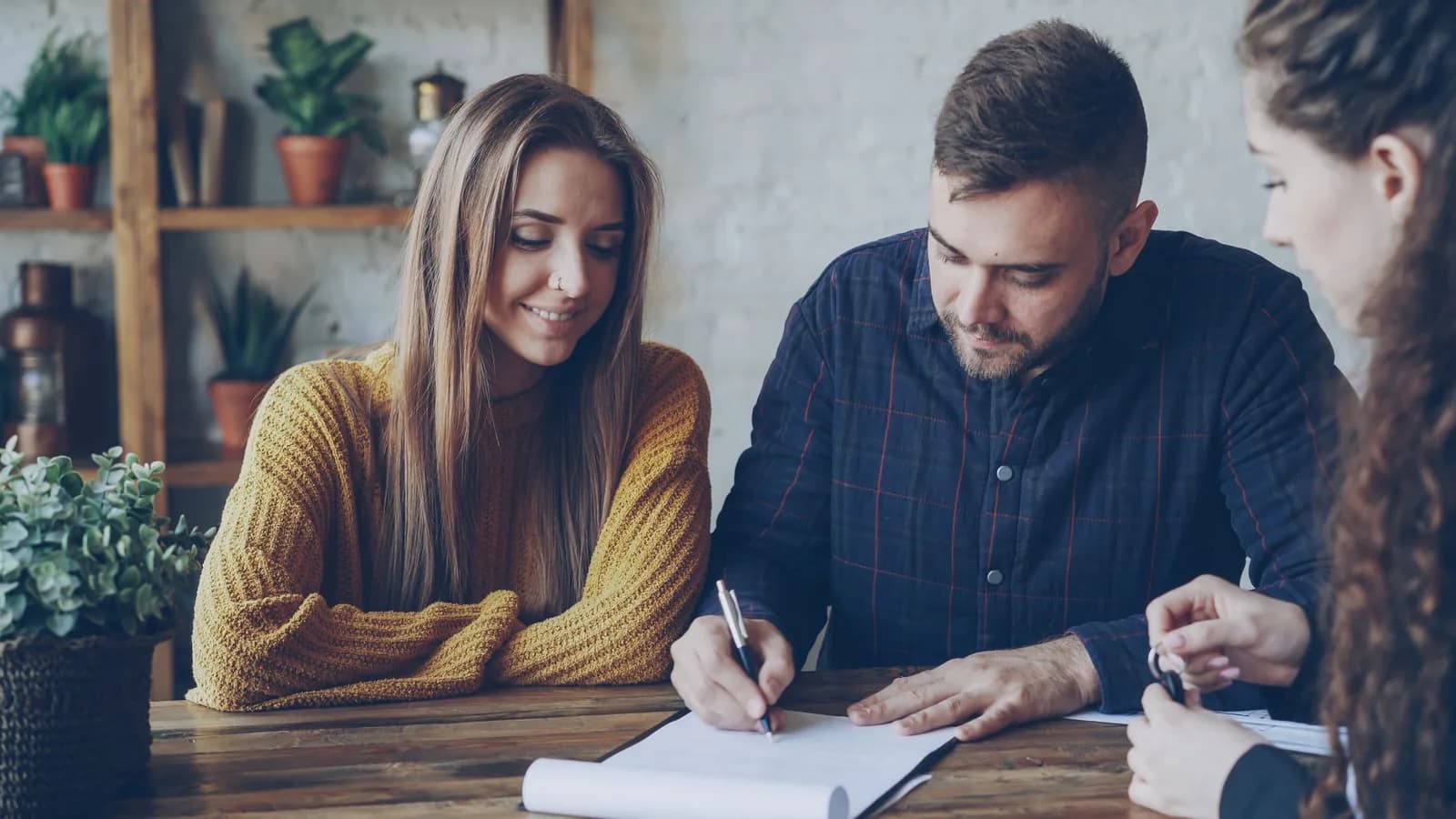 Un couple signe un contrat de vente avec un agent immobilier qui tient des clés