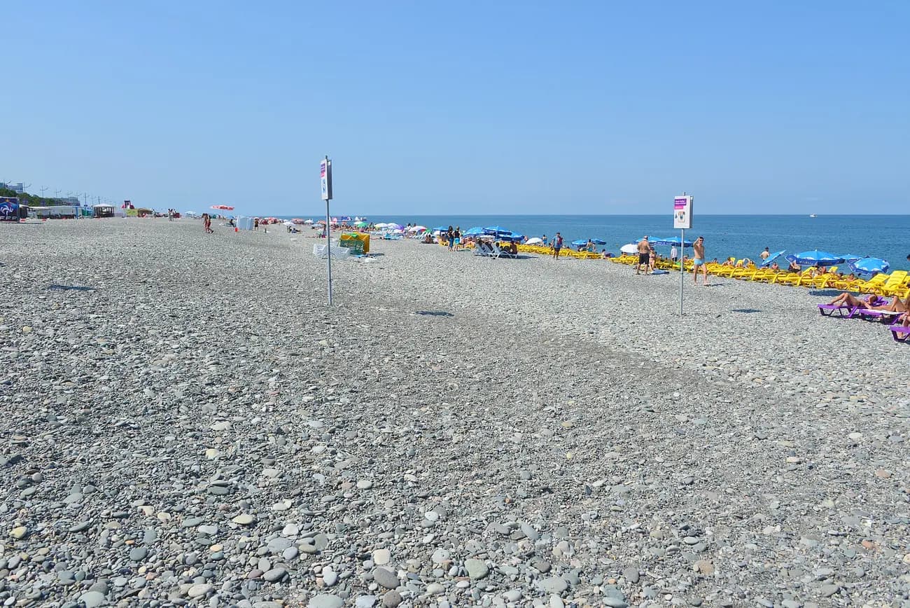 Plage de galets de Batoumi : large étendue de galets au premier plan, panneaux, parasols et transats jaunes en bord de mer