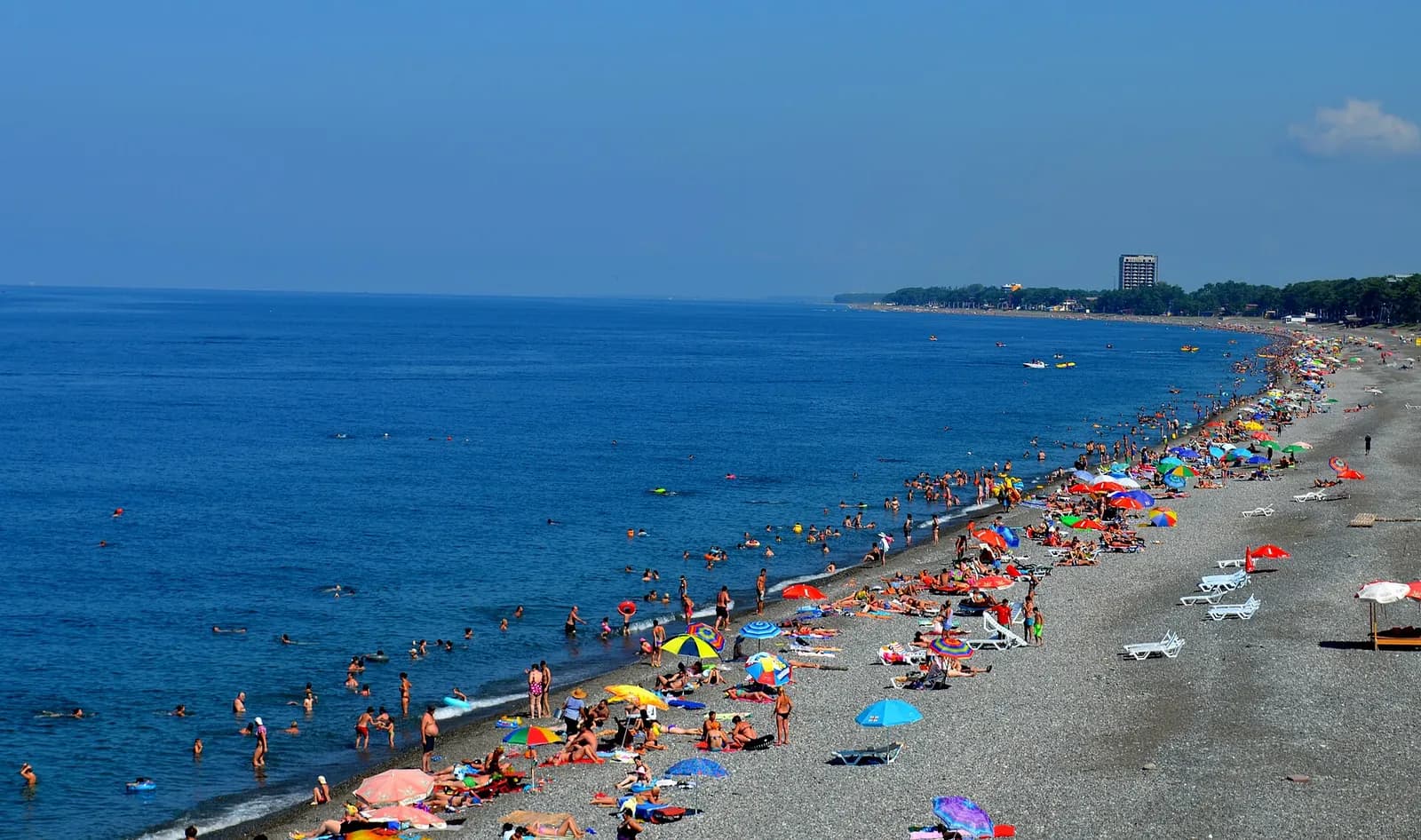Longue plage de galets de Kobuleti en été, baigneurs et parasols colorés