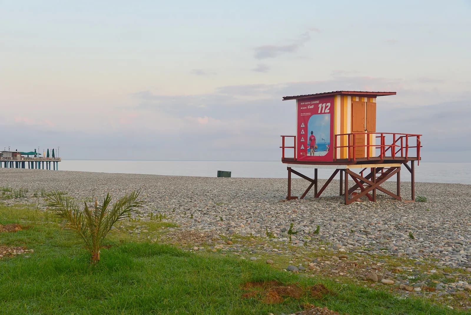 Poste de secours en bois sur la plage de galets de Batoumi, avec le numéro 112 et la jetée au loin