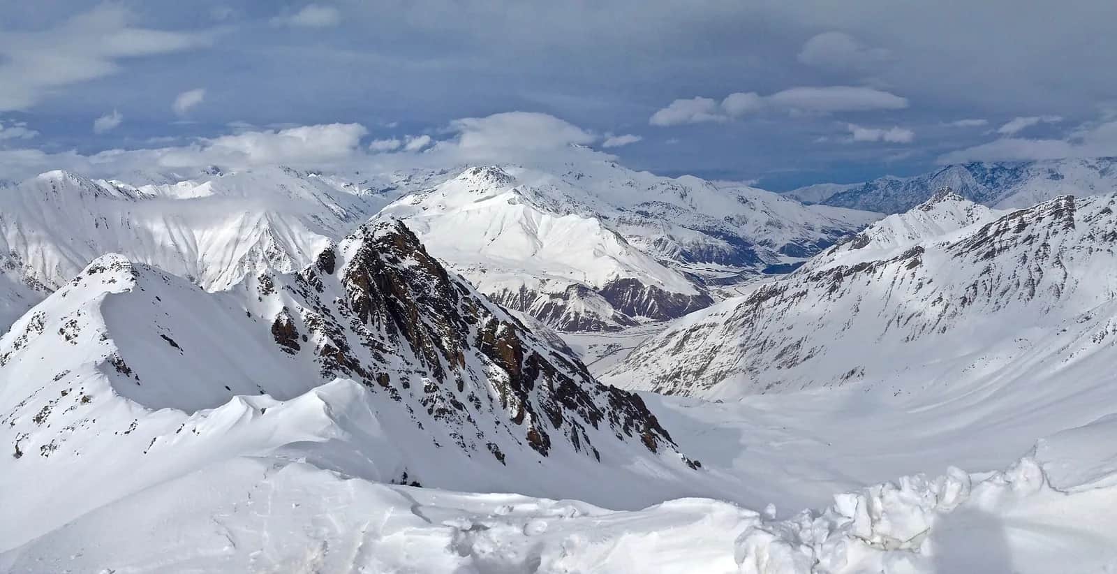 Panorama du Grand Caucase enneigé depuis les pistes de Gudauri, en Géorgie : crêtes rocheuses, vallées blanches et sommets sous les nuages