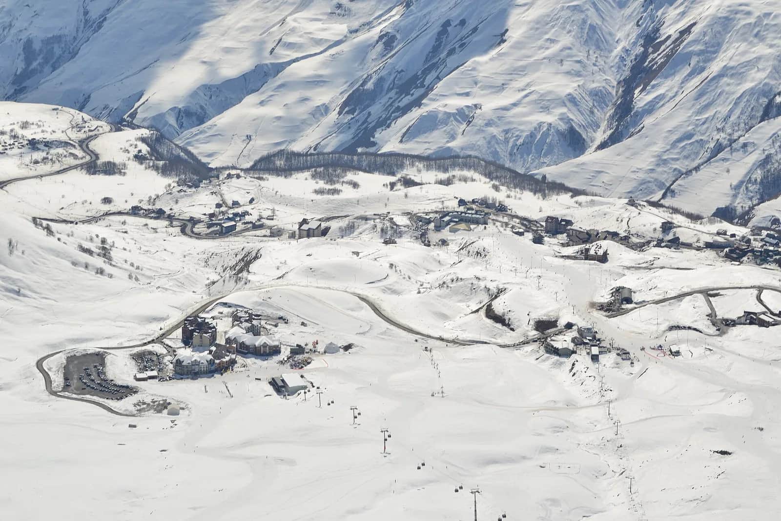 Vue aérienne de la station de Gudauri en hiver : hôtels, route en lacets, parking et télécabines sur les pistes enneigées