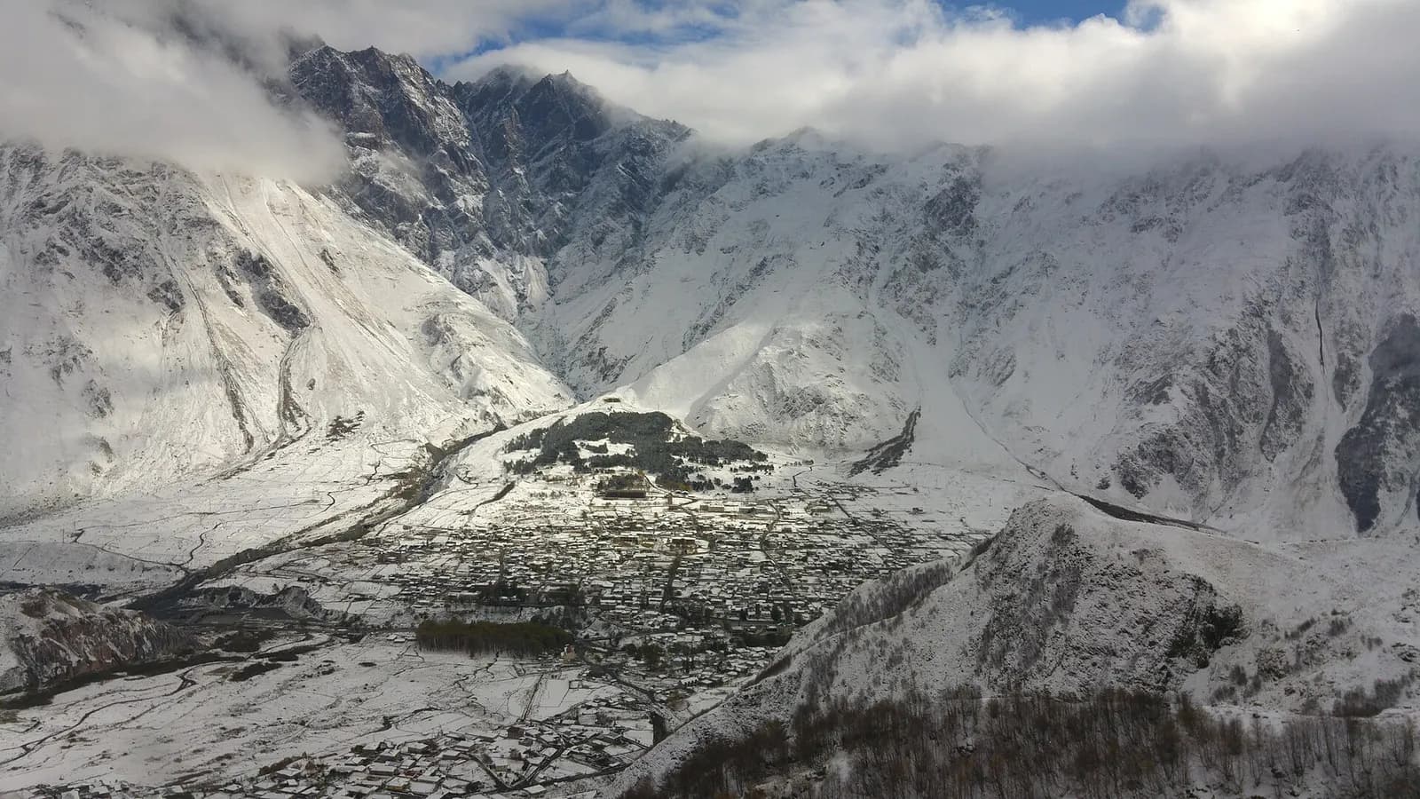 Stepantsminda sous la neige, vue depuis les hauteurs de l'église de Gergeti, avec les montagnes enneigées au fond