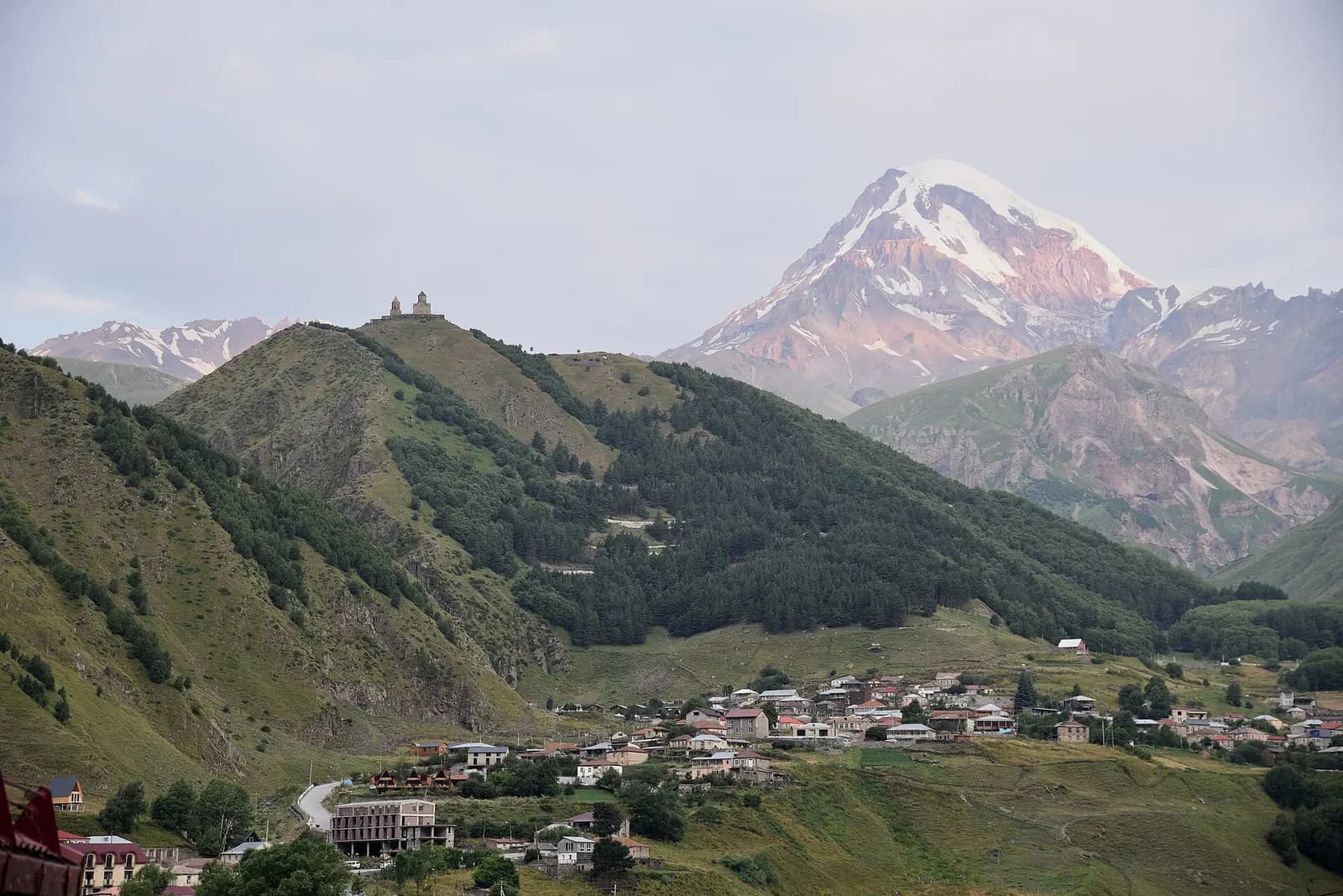 Le village de Stepantsminda dans la vallée, avec l'église de Gergeti sur la crête et le mont Kazbek au fond