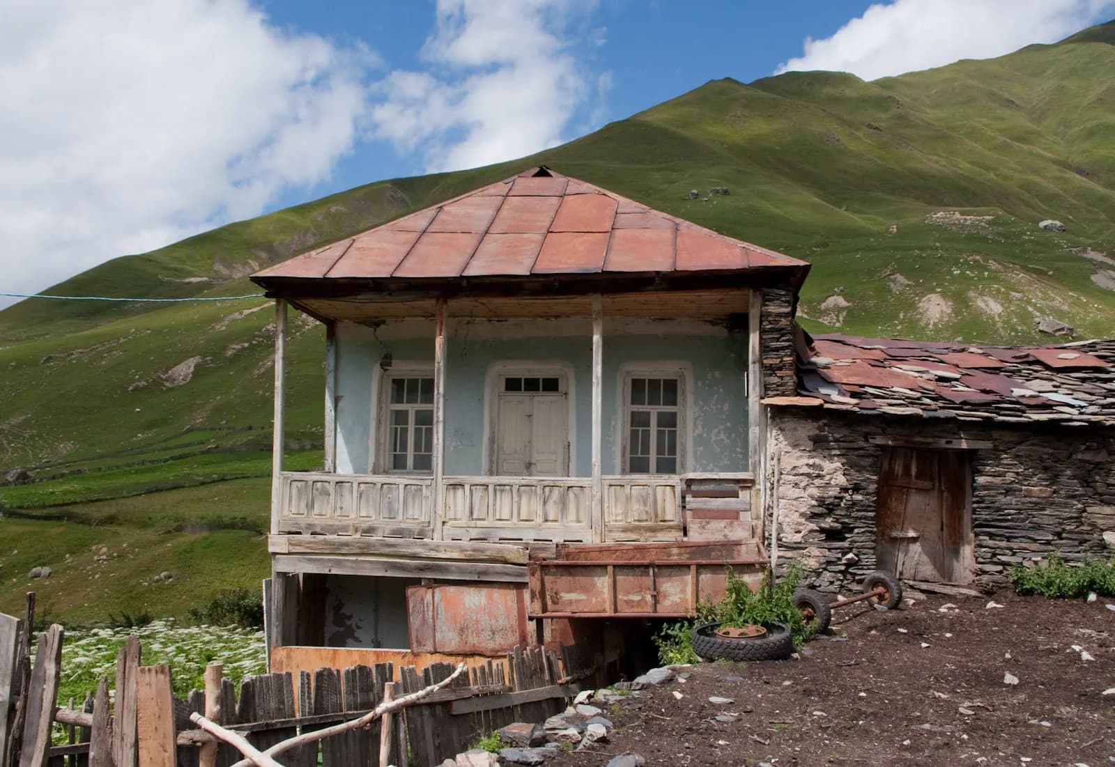 Maison traditionnelle à balcon de bois et toit de tôle, adossée à un versant herbeux à Ouchgouli, en Haute-Svanétie