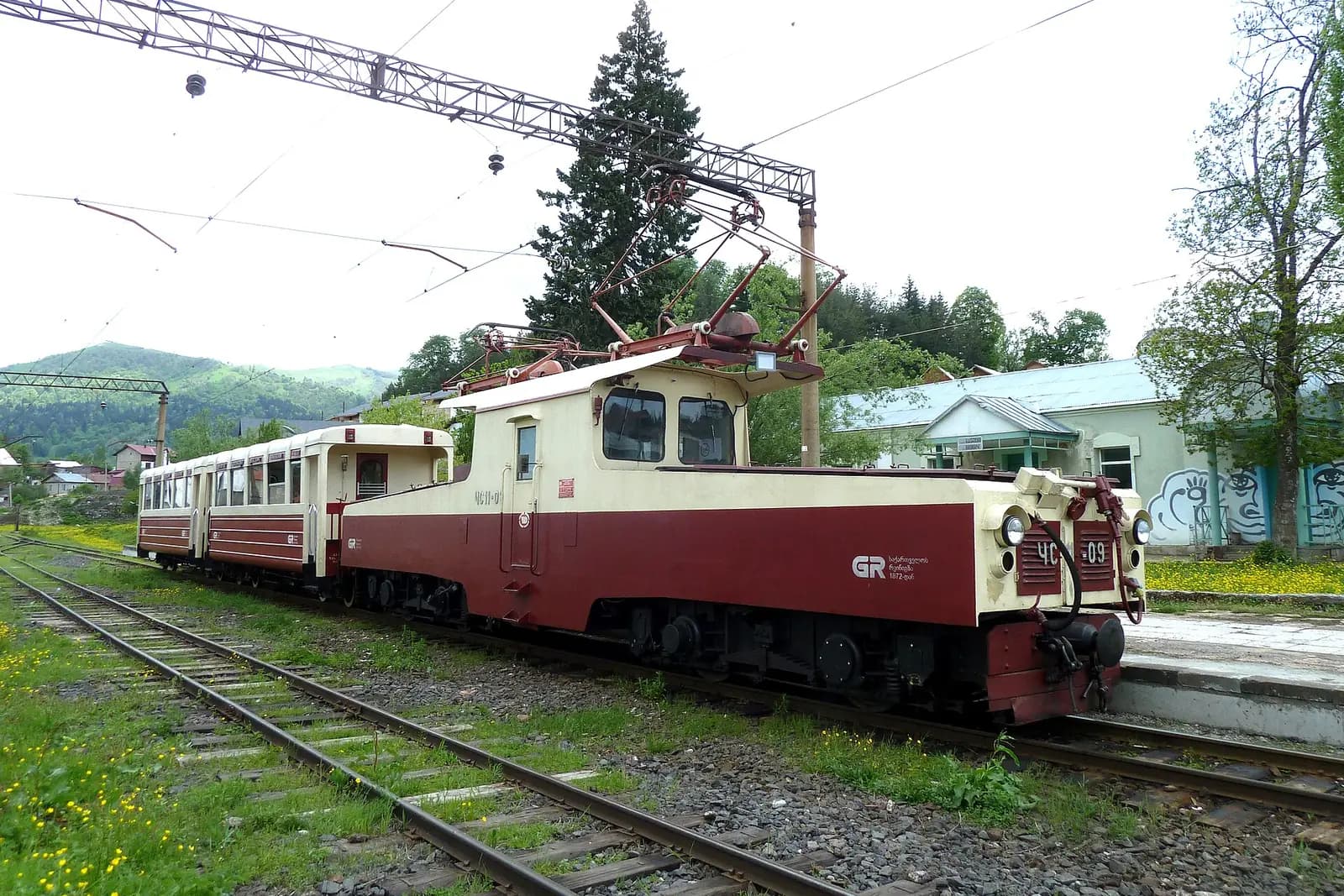 Petit train Kukushka rouge et crème de la ligne à voie étroite Borjomi-Bakuriani, à quai en gare de Bakuriani au milieu de la verdure