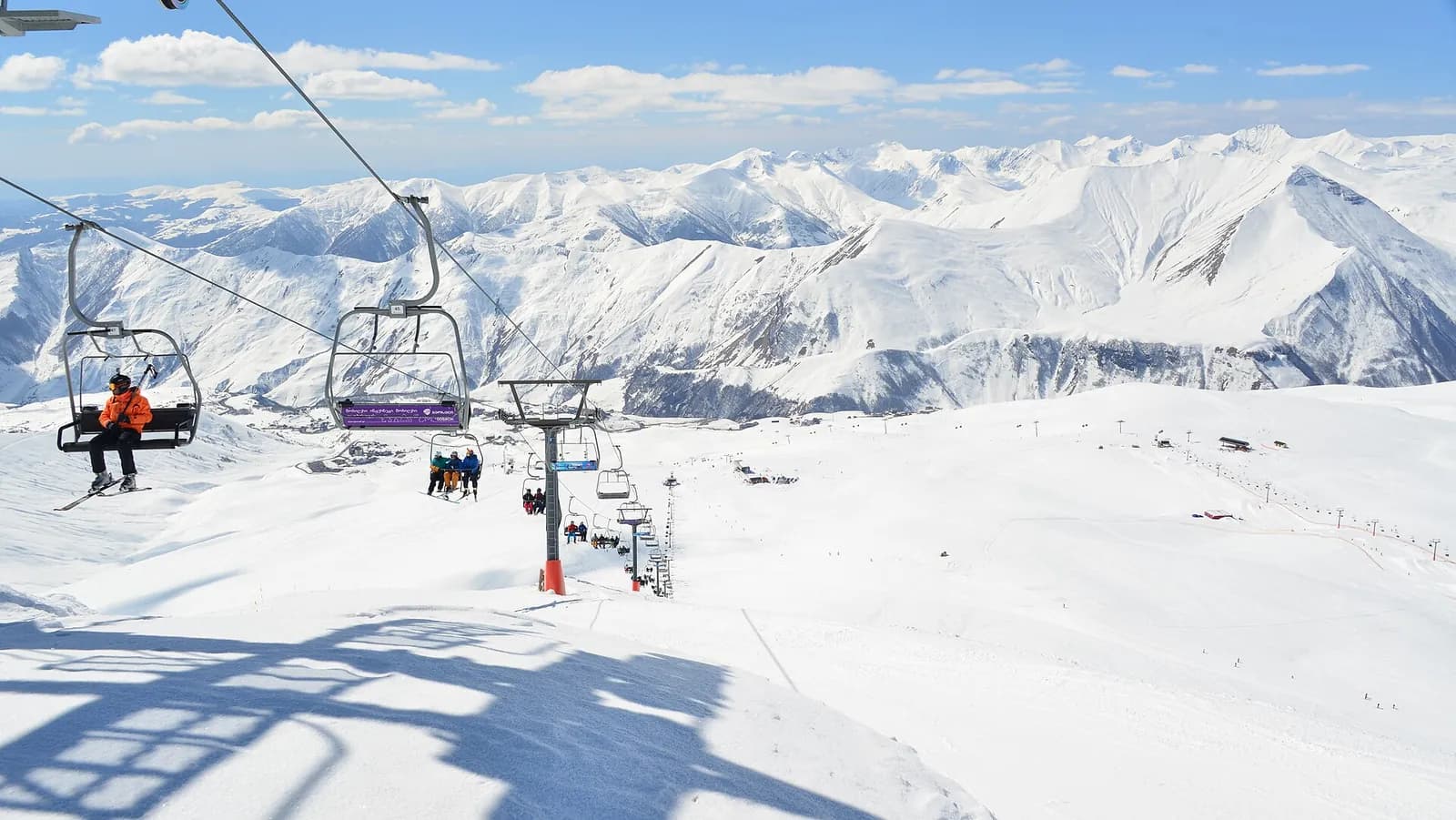 Télésiège au-dessus des pistes de la station de ski de Gudauri, avec un skieur et les crêtes enneigées du Grand Caucase en toile de fond