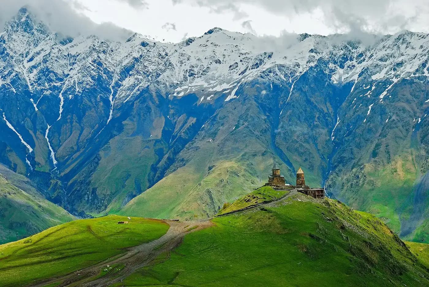 Église de la Trinité de Gergeti perchée sur sa colline verte, face aux sommets enneigés du Caucase au-dessus de Stepantsminda en Géorgie