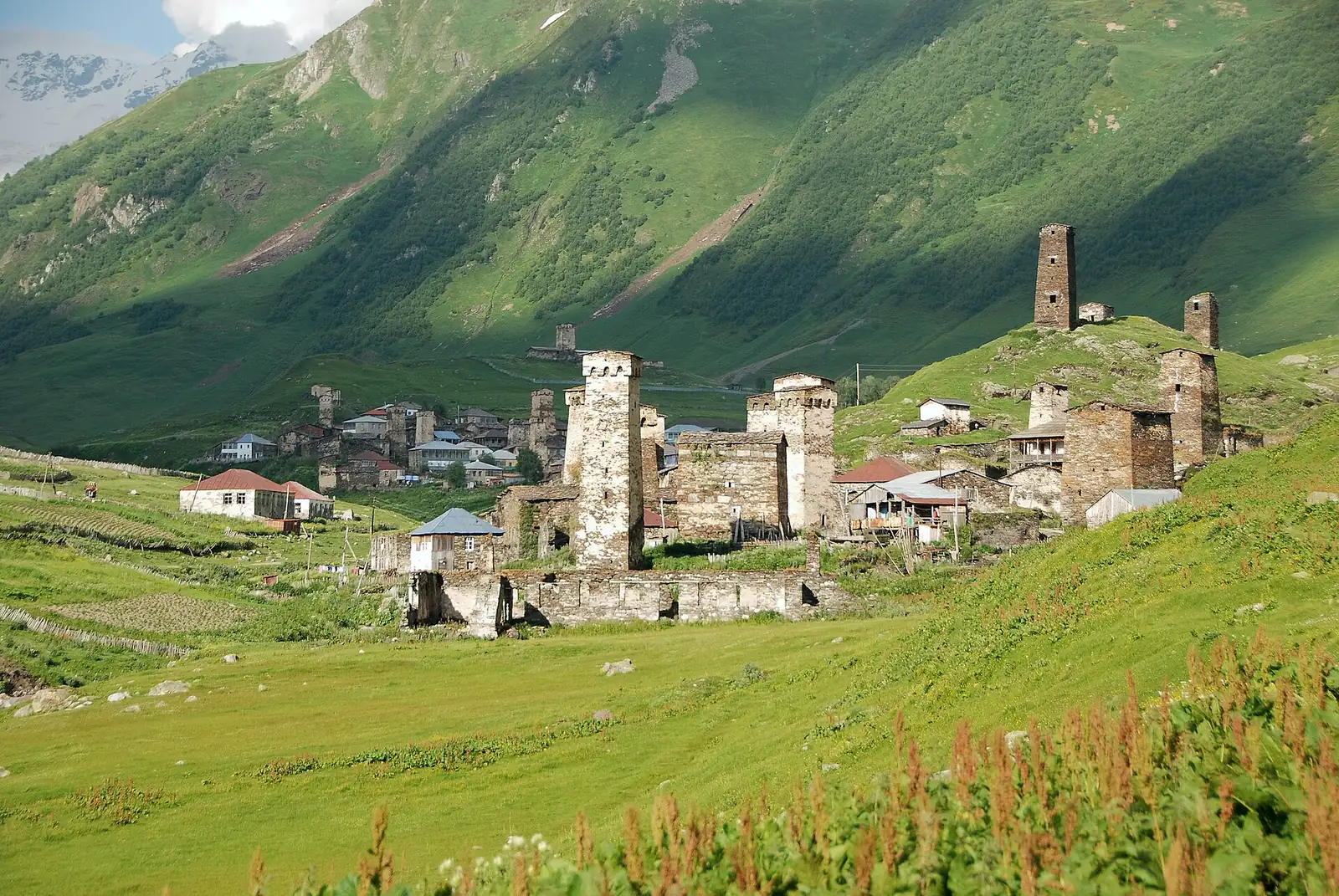 Village d'Ouchgouli en Svanétie : tours de pierre groupées au pied d'une colline éclairée par une lumière douce, versants verts de la vallée