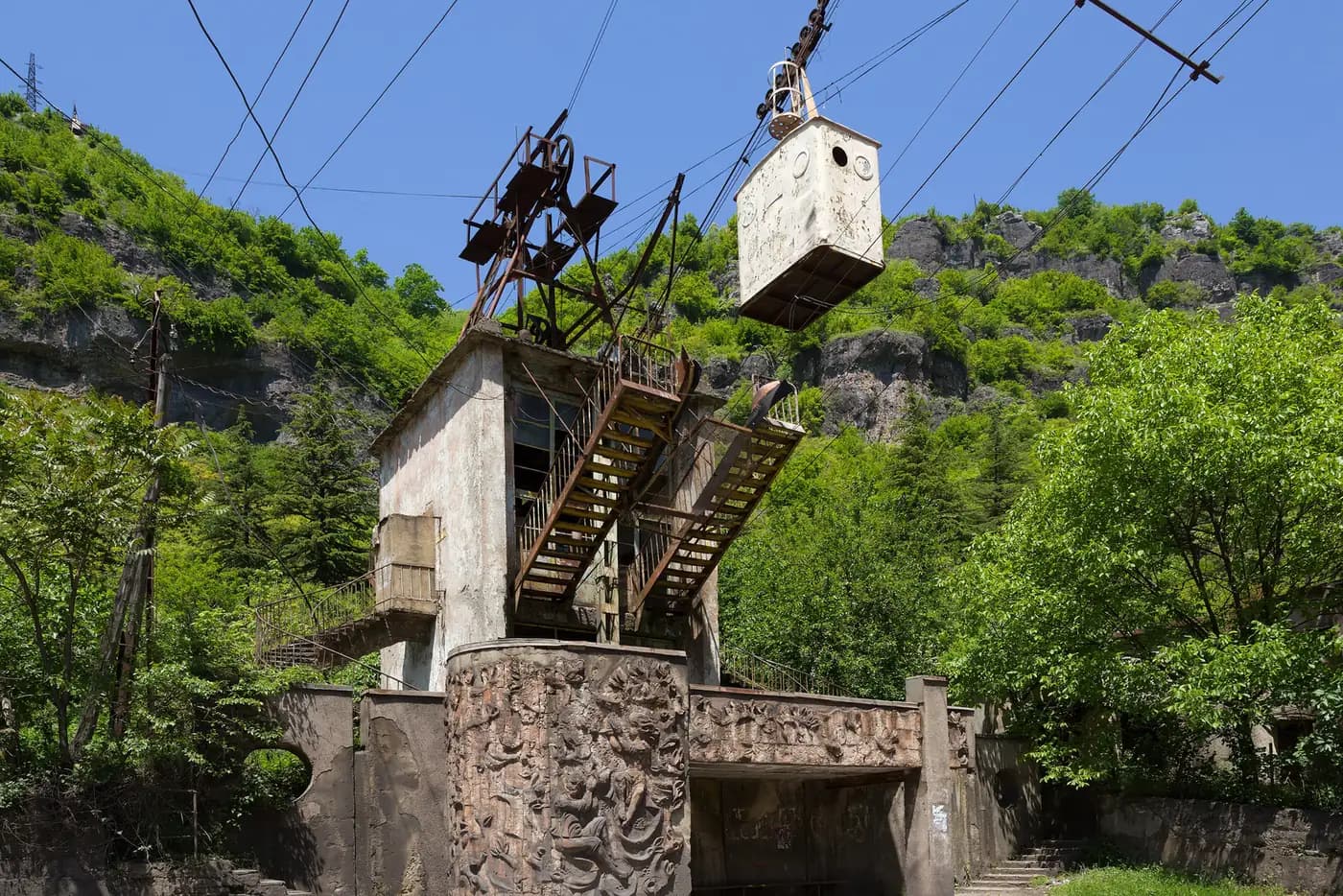 Ancienne gare de téléphérique soviétique à Tchiatoura, ornée de bas-reliefs, avec une cabine blanche suspendue au câble au pied de la falaise