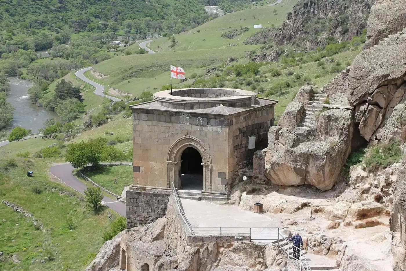 Édifice de pierre surmonté du drapeau géorgien sur les terrasses de la cité troglodytique de Vardzia, avec la route et la rivière dans la vallée en contrebas