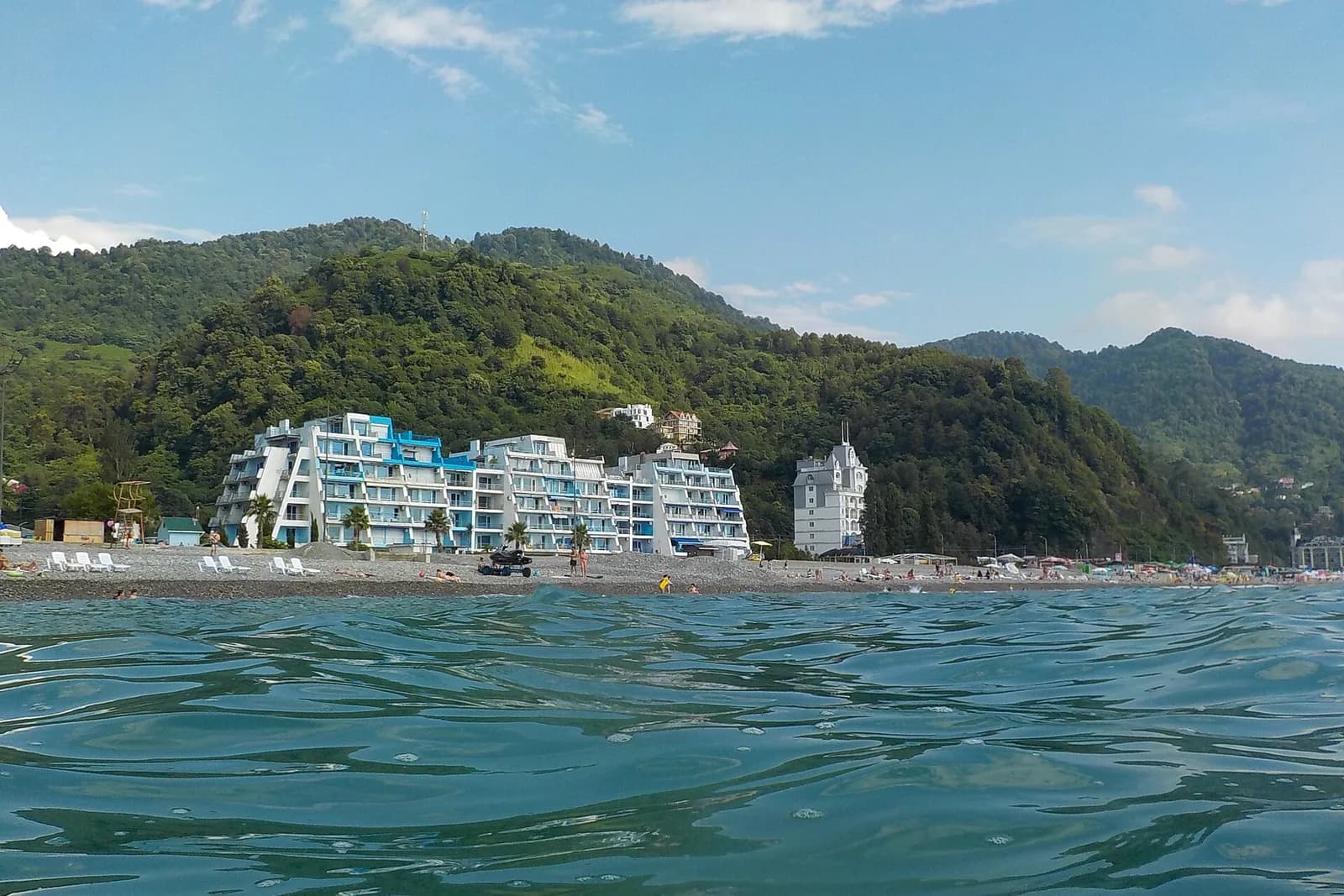 Plage de galets de Gonio vue depuis la mer, avec ses résidences blanches au pied des collines couvertes de forêt