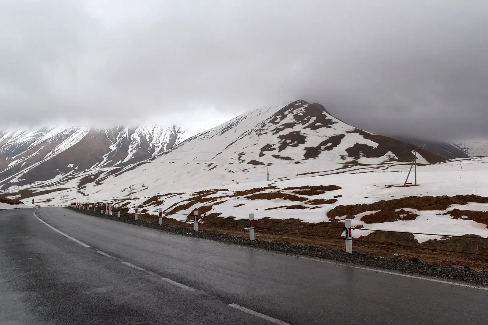 Route militaire géorgienne mouillée près du col de la Croix, entre névés et nuages bas