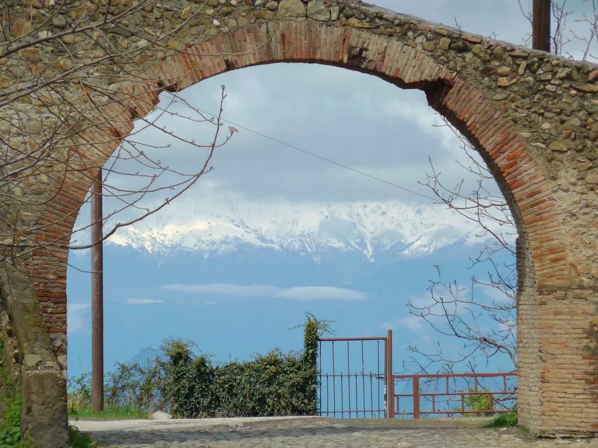 Vue de Signaghi à travers une arche de brique et de pierre : le Grand Caucase enneigé au-dessus de la vallée de l'Alazani