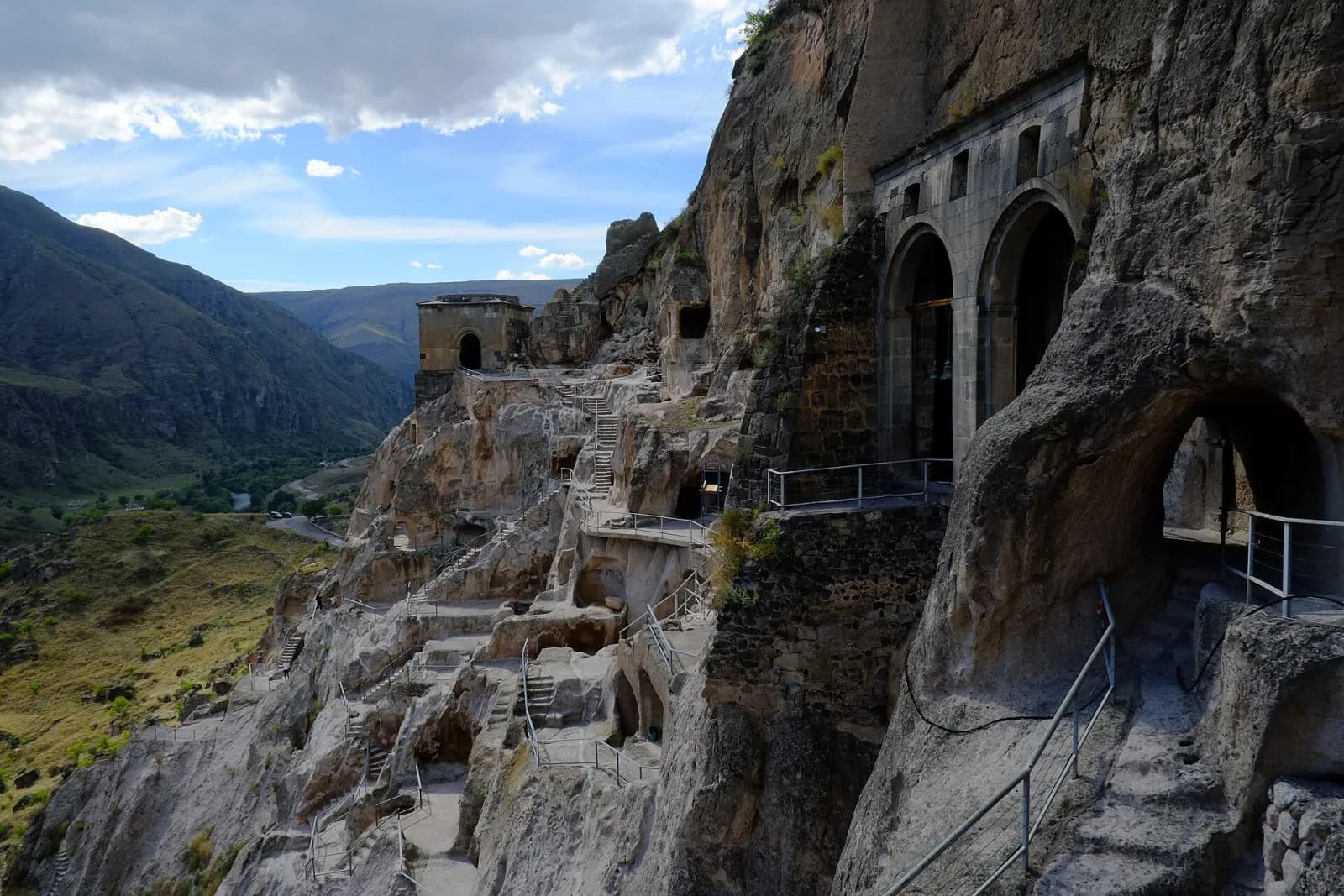 Escaliers, passerelles et galeries taillés dans la roche à Vardzia, avec le clocher de l'église de la Dormition et la vallée en contrebas