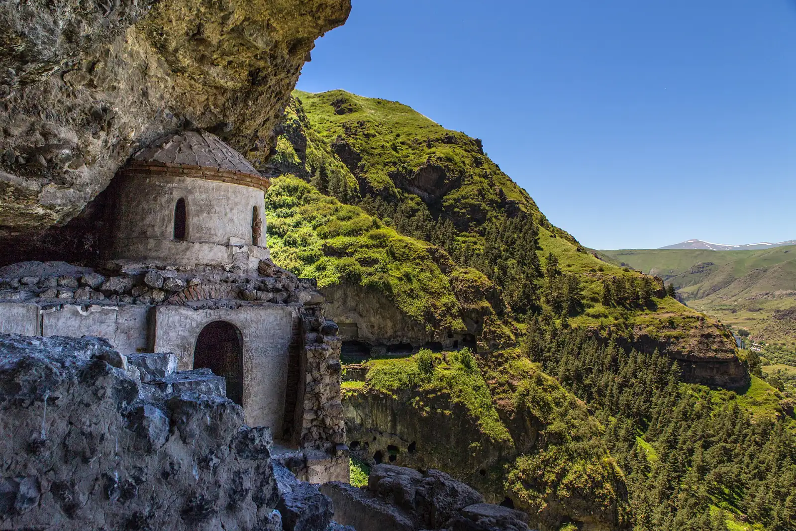 Petite église sous un surplomb rocheux au monastère rupestre de Vanis Kvabebi, avec les galeries creusées dans la falaise et la vallée de la Koura